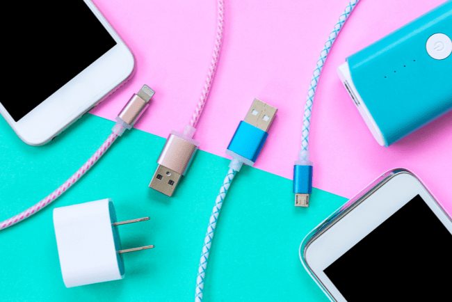 USB-kablar till smartphones i olika färger. Två smartphones och en bärbar mobilladdare.