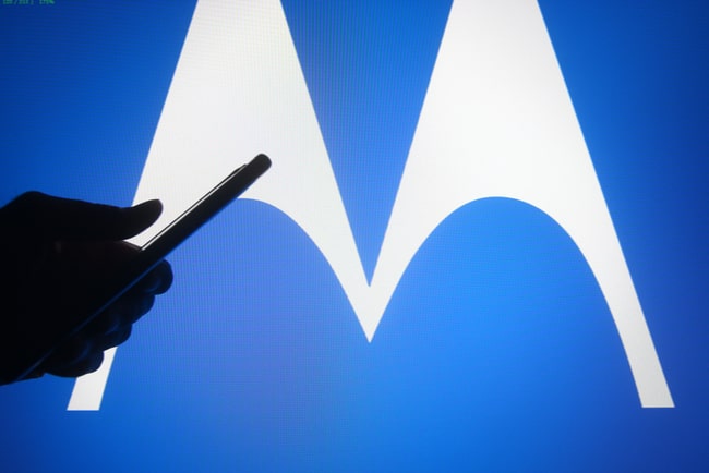 Motorolas logga i bakgrunden med en siluett av en hand med mobil i förgrunden.